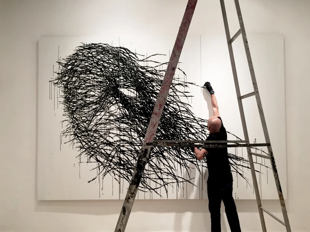 Yuri Leonardo on a ladder, painting a large black mural on a white wall